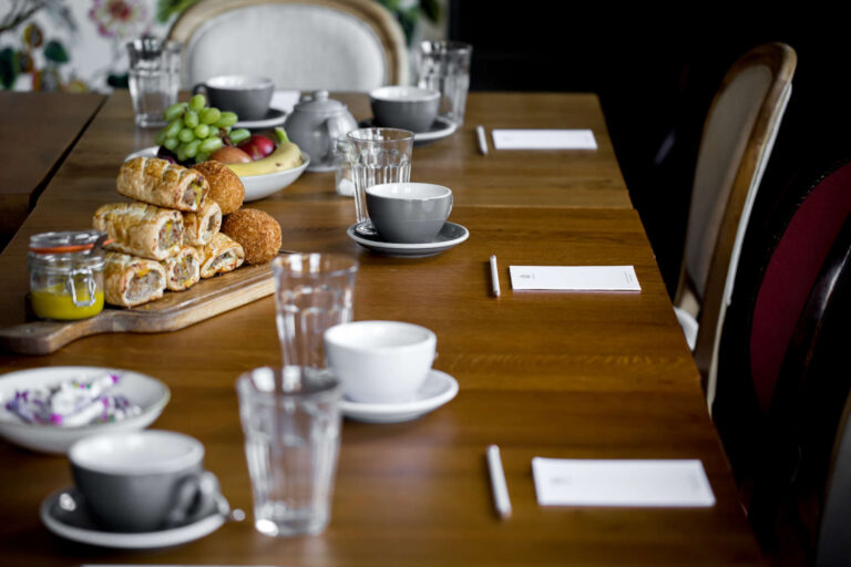 Meeting room set up with snacks, coffee cups, water glasses, and paper